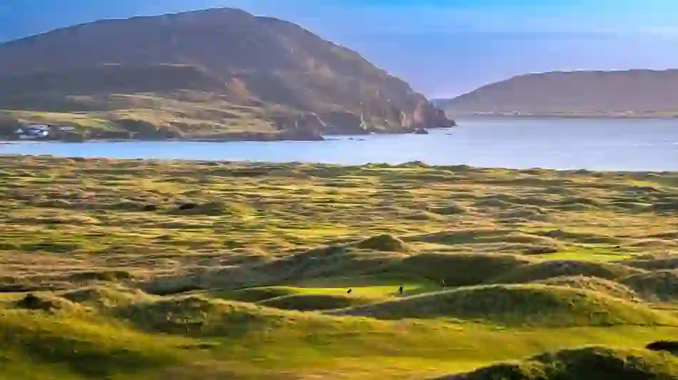 Golfers playing on the links at Ballyliffin Golf Club with rugged coastline in County Donegal.