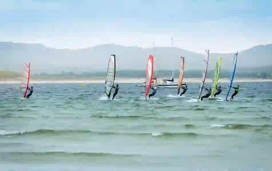 Windsurfers glide across choppy waves near the coast in County Donegal, with sails lit by soft summer light.