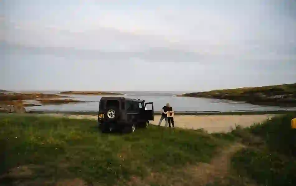A couple embraces beside a black jeep parked on a quiet beach cove at Crookhaven, Cork.