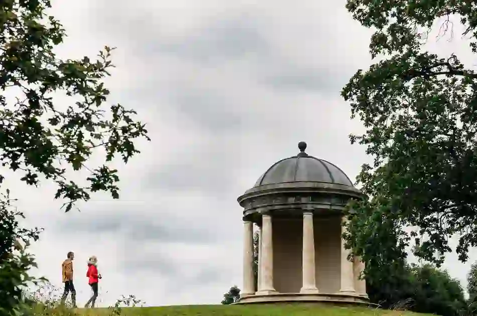 Two people walking beside a classical domed temple with columns in parkland at Castletown House, County Kildare.