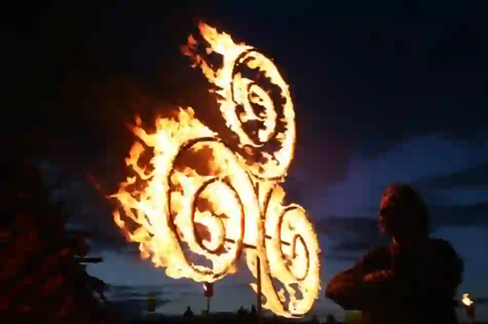 Silhouette of a person beside a Celtic spiral design burning brightly at night on the Hill of Uisneach, County Westmeath.