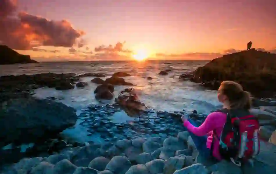 Traveller watching sunset over the sea from the basalt rocks of the Giant’s Causeway in Antrim.