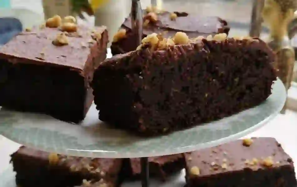 Rich chocolate brownies topped with walnuts on a cake stand.