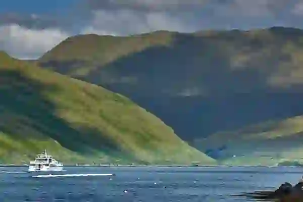 Tour boat on Killary Harbour in County Galway with green mountains rising steeply on either side under cloudy skies.