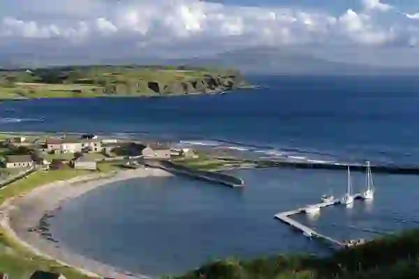 Small marina with yachts docked at Rathlin Island Harbour, Antrim, set beside curved beach and rugged coastal cliffs.