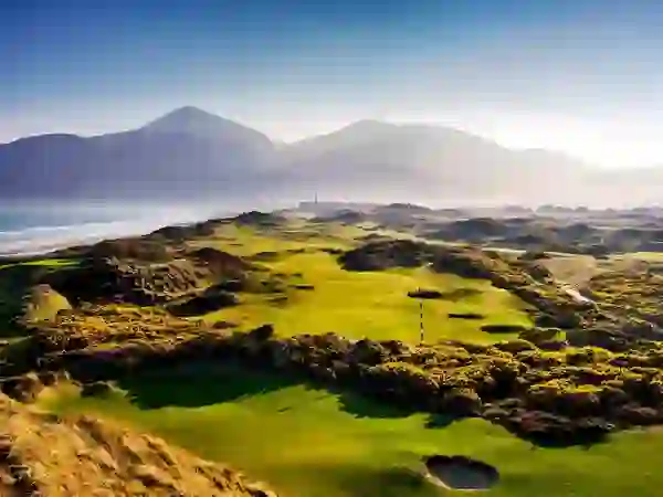 Expansive fairways of Royal County Down Golf Club with Mourne Mountains in the distance and coastline along the left.