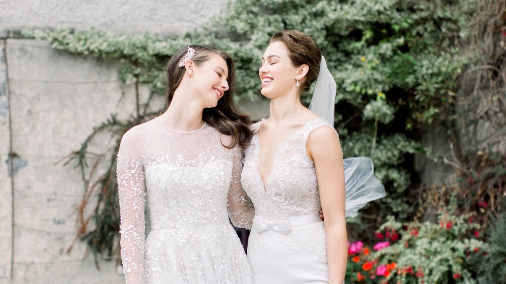 Two brides smiling at each other in wedding dresses outside, highlighting Ireland wedding tips for same-sex couples.