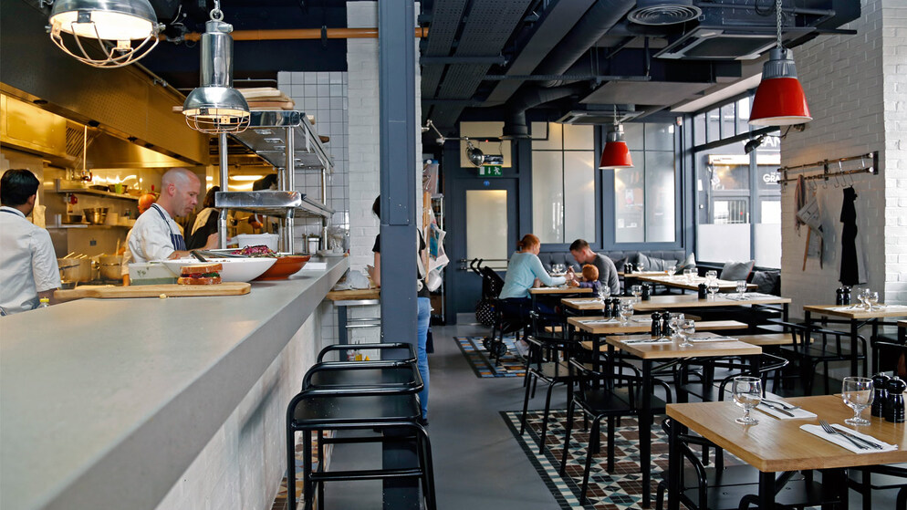 Open-plan Irish restaurant with chefs at work and diners at wooden tables.